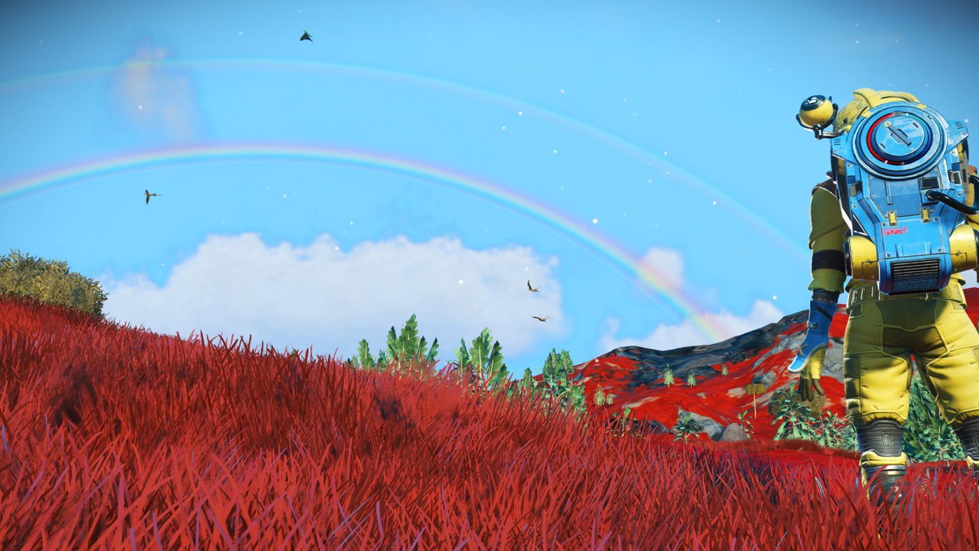 No Man's Sky: an astronaut at the edge of the frame on a red hillside under a rainbow and flying creatures