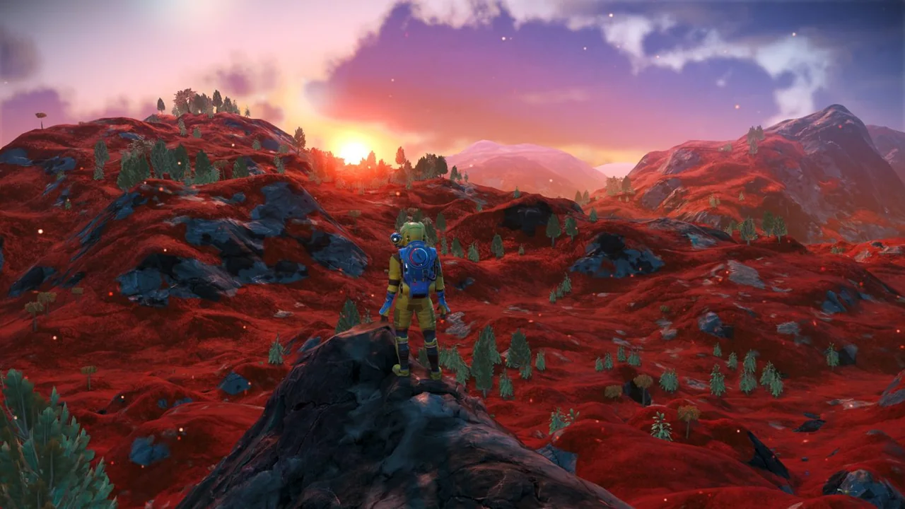 No Man's Sky: an astronaut in a yellow suit standing on a dark rock above red hills with the sun setting behind